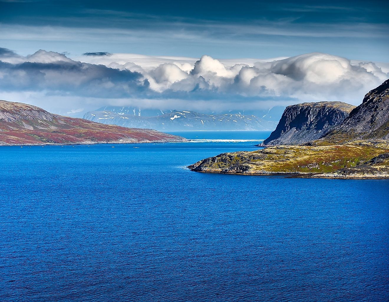 The remote Bering Strait near Alaska features cold deep blue water, rugged northern mountains, dramatic clouds and pristine Arctic wilderness.
