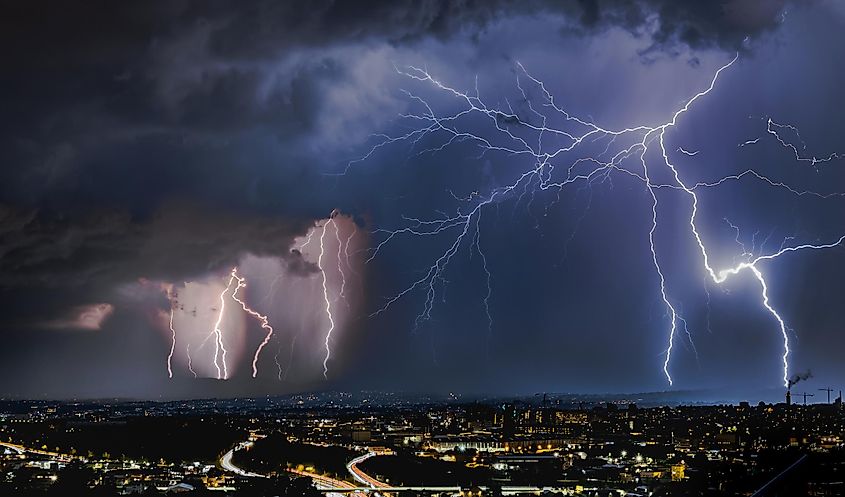 A thunderstorm with lightning striking over a city skyline at night.