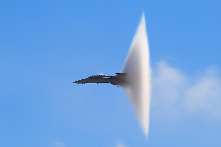 A military jet trailing a cone-shaped vapor cloud during high-speed flight.