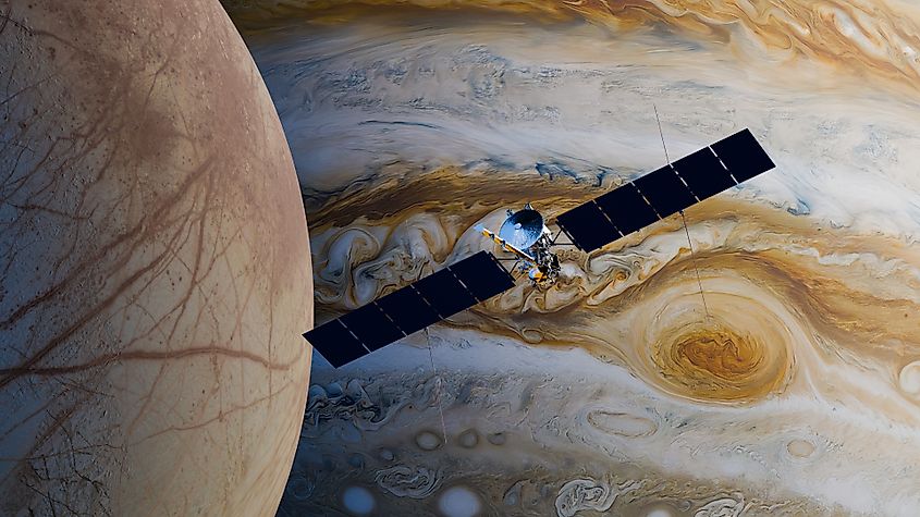 Illustration of the Europa Clipper spacecraft passing over Europa with Jupiter behind