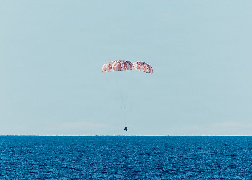 The Orion space craft parachutes toward the ocean. 