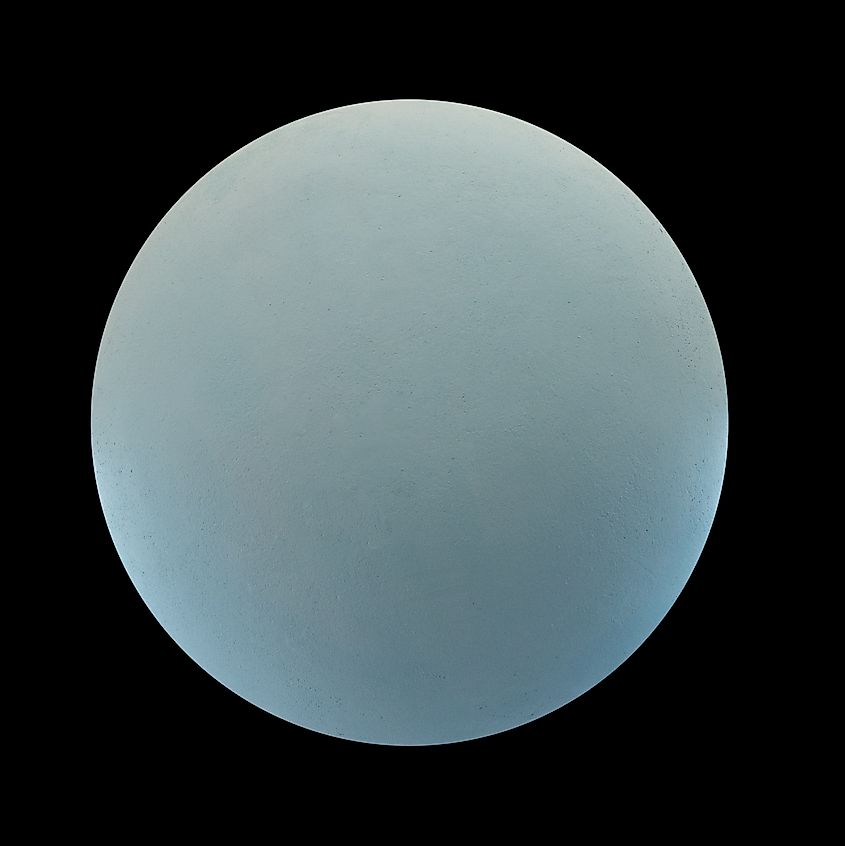 The pale blue-green disc of the planet Uranus isolated against black space.