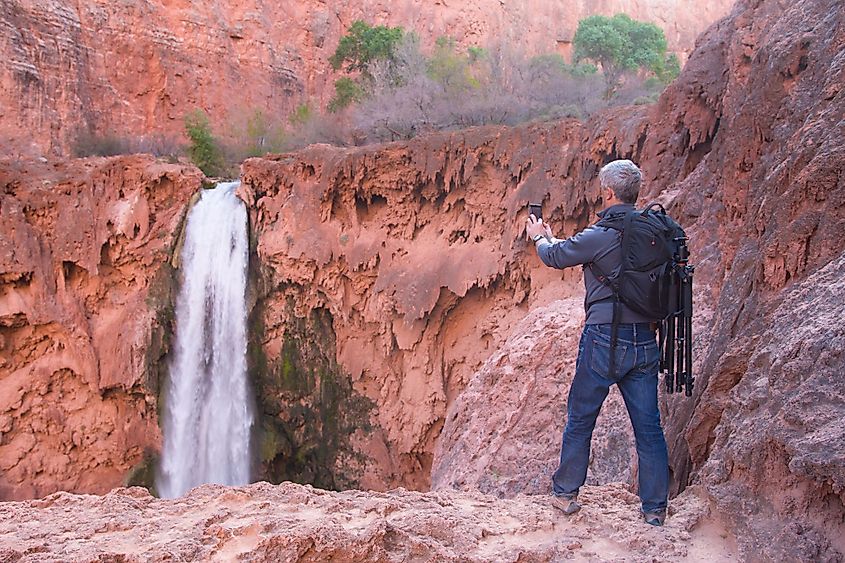 Man with photo gear takes picture of Mooney Falls with his mobile phone, Havasu Canyon, Arizona, USA. Via Shutterstock / Kira Volkov